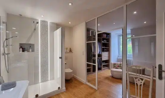 Salle de bain avec douche et wc suspendu, avec une paroi verrière la séparant d'un dressing parental